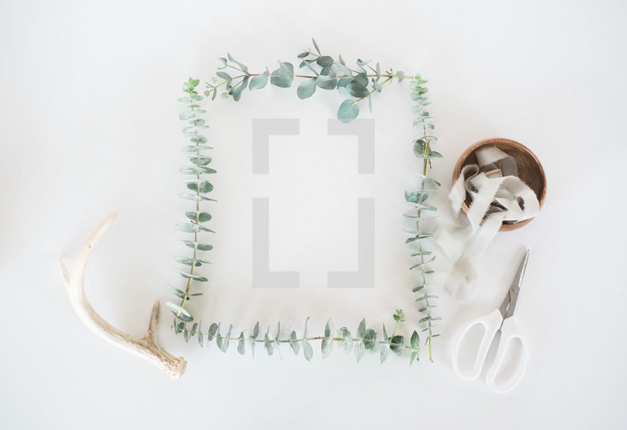 eucalyptus frame, antlers, scissors, and spool of ribbon in a bowl 