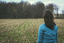 a woman standing in front of a plowed field 
