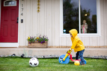 Child playing with soccer ball and bike in front yard. 