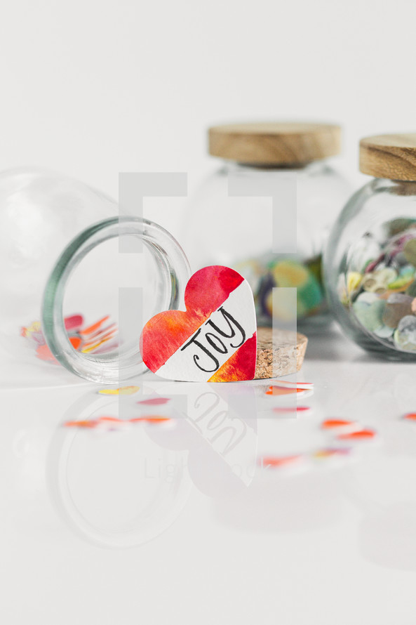 Jars of paper hearts on a white background with one lettered JOY in front.