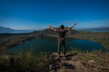 a man standing on an island mountaintop looking out with hands raised 