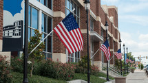 row of American flags on flag poles along a sidewalk 