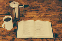 coffee mug, creamer, open Bible on wood table 