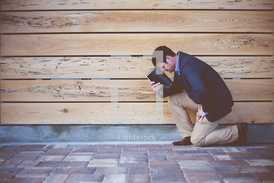 man kneeling in prayer holding a Bible 