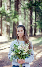 a woman holding a bouquet of flowers in the woods 
