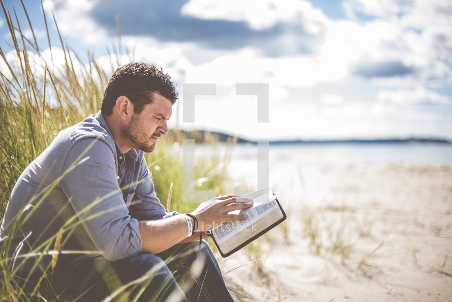man reading a Bible on a beach 