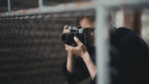a woman taking a picture through a chain link fence 