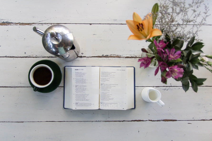 coffee, flower vase, and open Bible on a wood table 