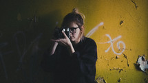 a woman holding a camera standing in front of a graffiti covered wall 