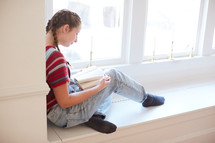 girl sitting in a window seat reading a book 