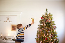 young kid reaching to put a star on the Christmas tree