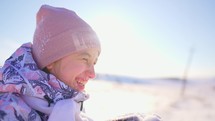 Happy child girl plays with a snow in winter day. Girl enjoys winter, frosty day. A young girl throws up snowflakes in the bright sun. Snowflakes fly at sun light. Slow motion.