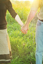 Couple holding hands while standing in tall grass.