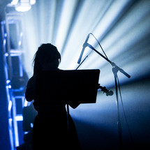 A silhouetted woman playing the violin on stage