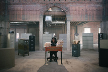 an overworked woman standing behind a desk covered in files 