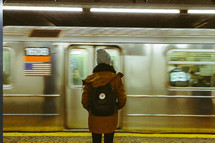 woman standing in a subway in front of a passing subway train 