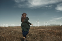 a woman running in a field near a wind farm 