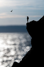 silhouette of a person standing at the edge of a cliff over the ocean 