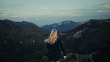 a woman in a plaid shirt looking out at a mountain view 