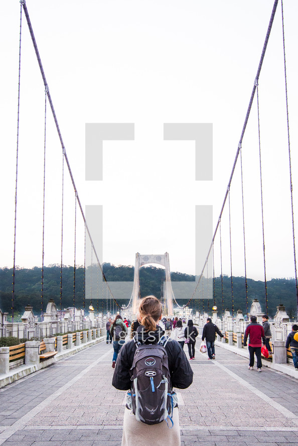 people with backpacks crossing over a bridge 