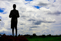 Silhouette of boy standing in field with cloudy sky in the background.