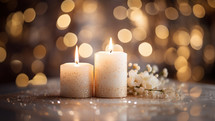 Natural burning candles with glitter around them and a small branch with white flowers. in the background, we see fairy lights, 