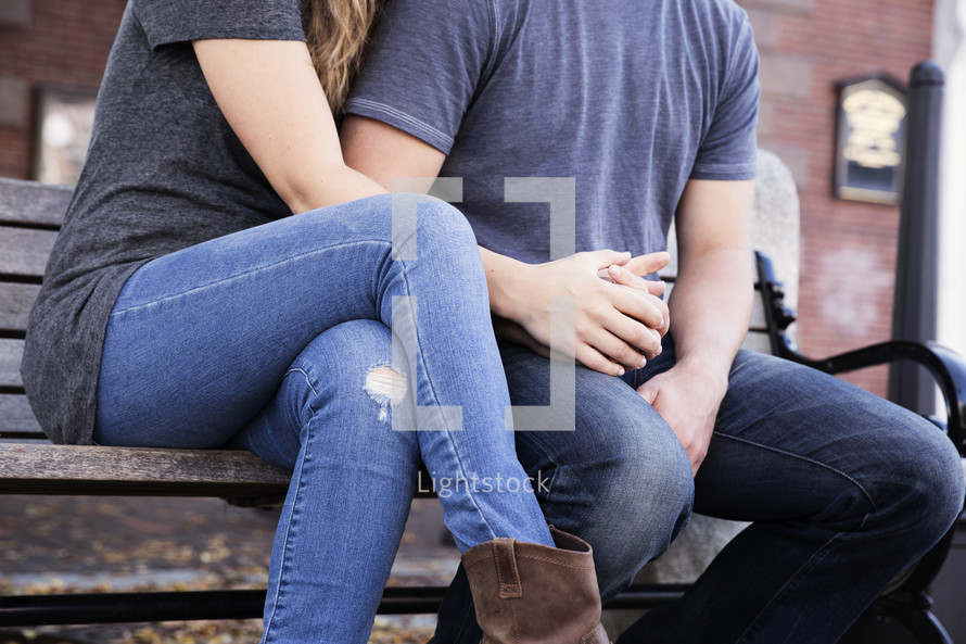 a couple snuggling sitting on a park bench 