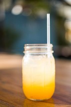 Mason jar filled with ice and juice with a straw.