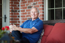 a smiling man sitting on a porch relaxing 