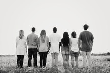 group of young adults standing outdoors with backs to the camera 
