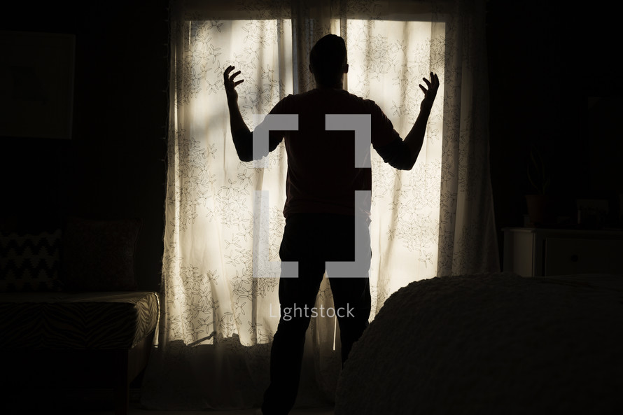 silhouette of a man standing in a window with raised hands 