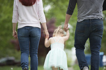 a mother, father, and toddler girl walking holding hands 