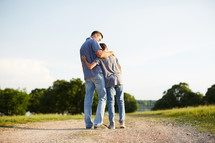 a father and son hugging standing on a dirt road 