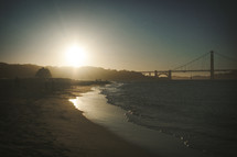 tide washing onto a shore and a bridge over a bay