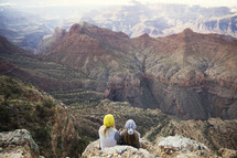 friends sitting on a mountainside cliff looking out at a canyon