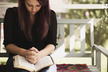 woman reading a Bible and praying on her front porch swing 