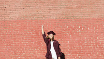 smiling female graduate standing in front of a brick wall 