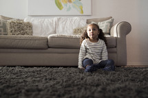 a girl child sitting on a rug in a living room 