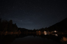 stars in a night sky over a mountain lake and lights from cabins 