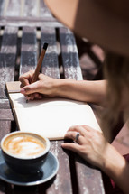 a woman writing in a journal over coffee 