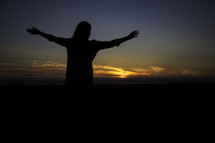 Silhouette of a woman with arms raised towards the sunset.