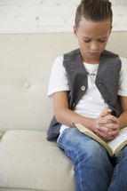 a boy child with praying hands over the pages of a Bible 