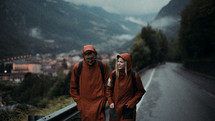 a man and woman in rain gear walking down a mountain road 
