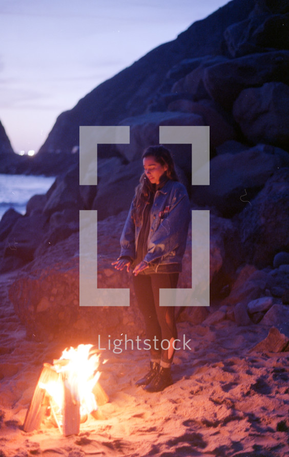 a woman standing by a fire on the beach 