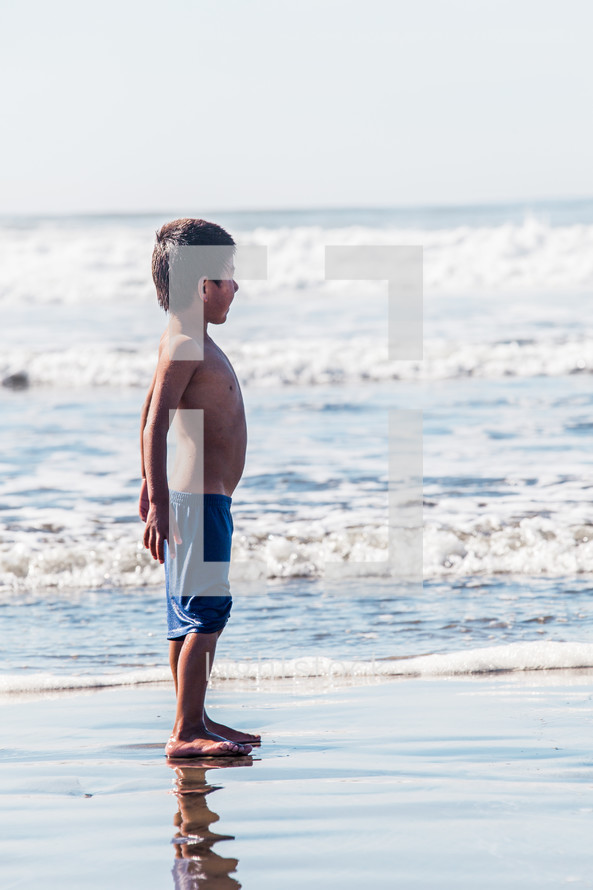 boy child standing on wet sand on a beach 