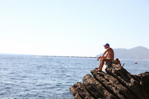 A fisherman sitting on a rock fishing