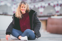 Curly haired blonde woman sitting on beach. Casual clothes