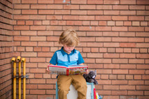 a child reading a book sitting on a locker 
