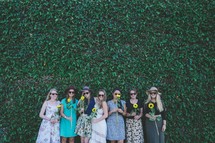 women holding sunflowers in front of an ivy wall