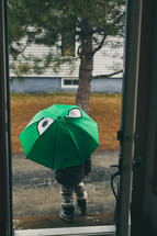 a child with an umbrella and snow boots walking out the front door